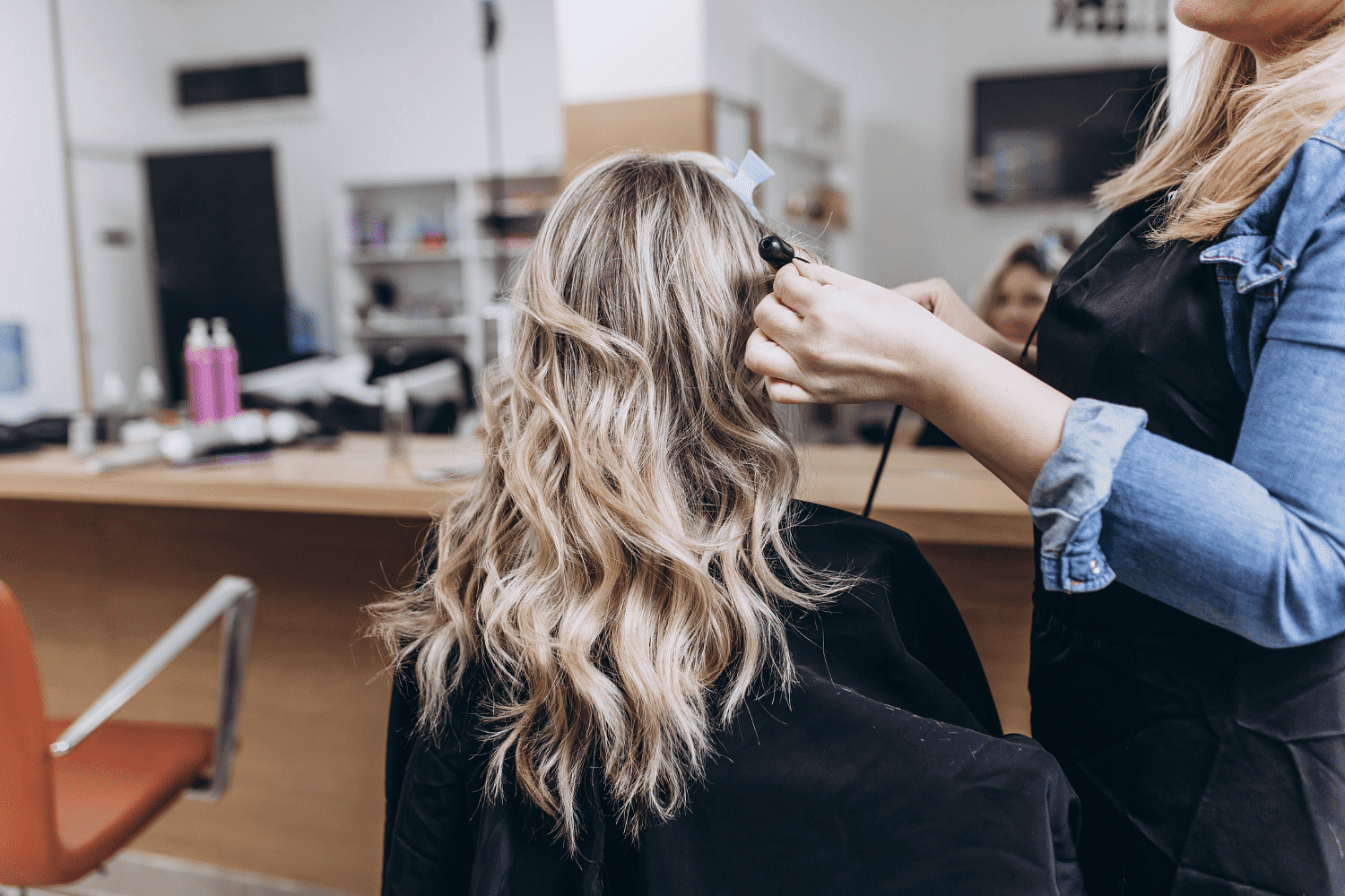 Hairdresser styling a woman's blonde hair with a curling iron in a salon.