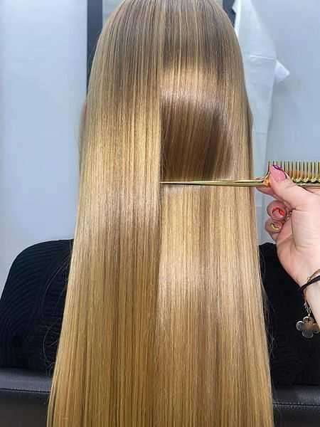 Hairdresser combing long, straight, blonde hair in a salon.