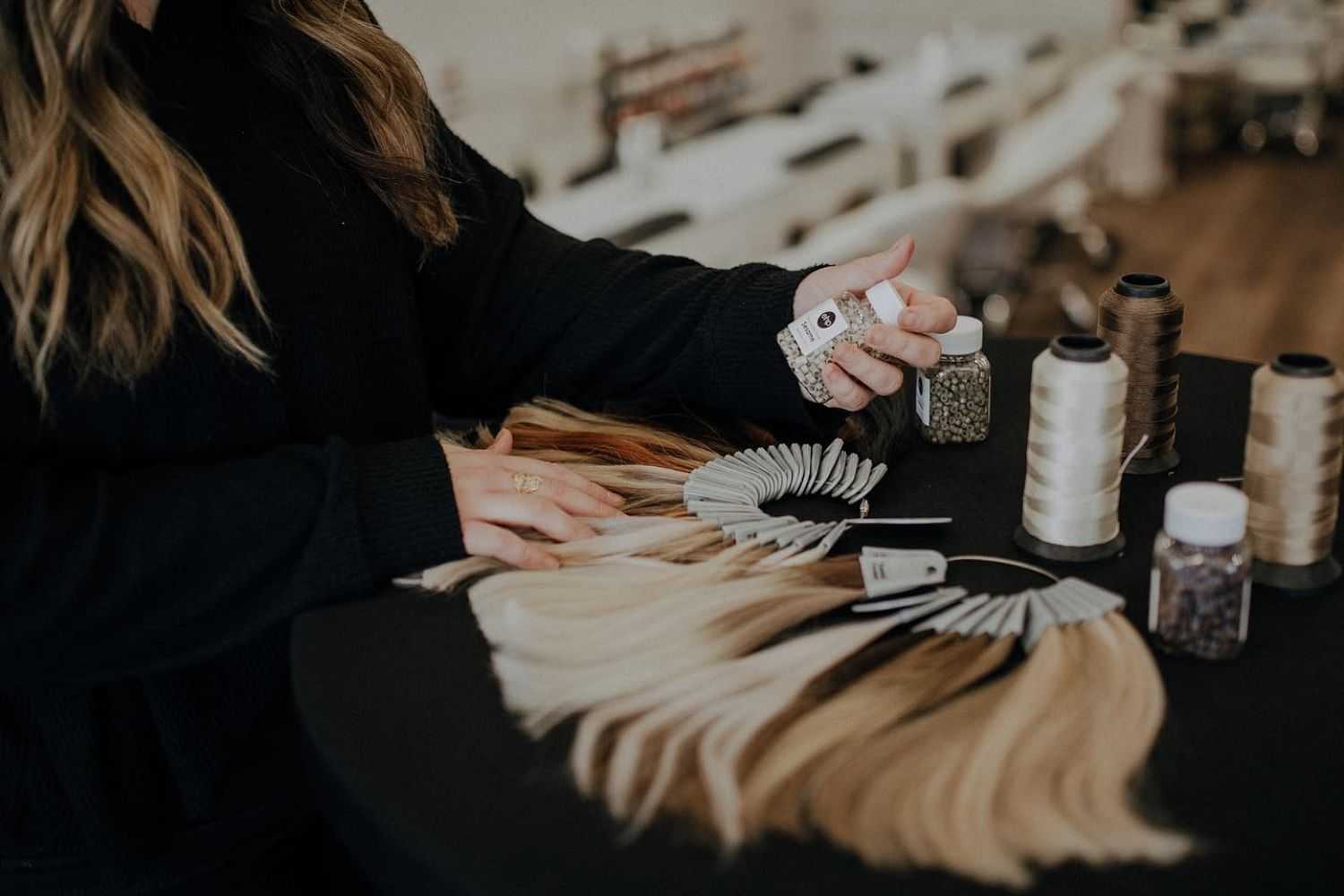 Person arranging hair extensions and color swatches on a table in a salon.