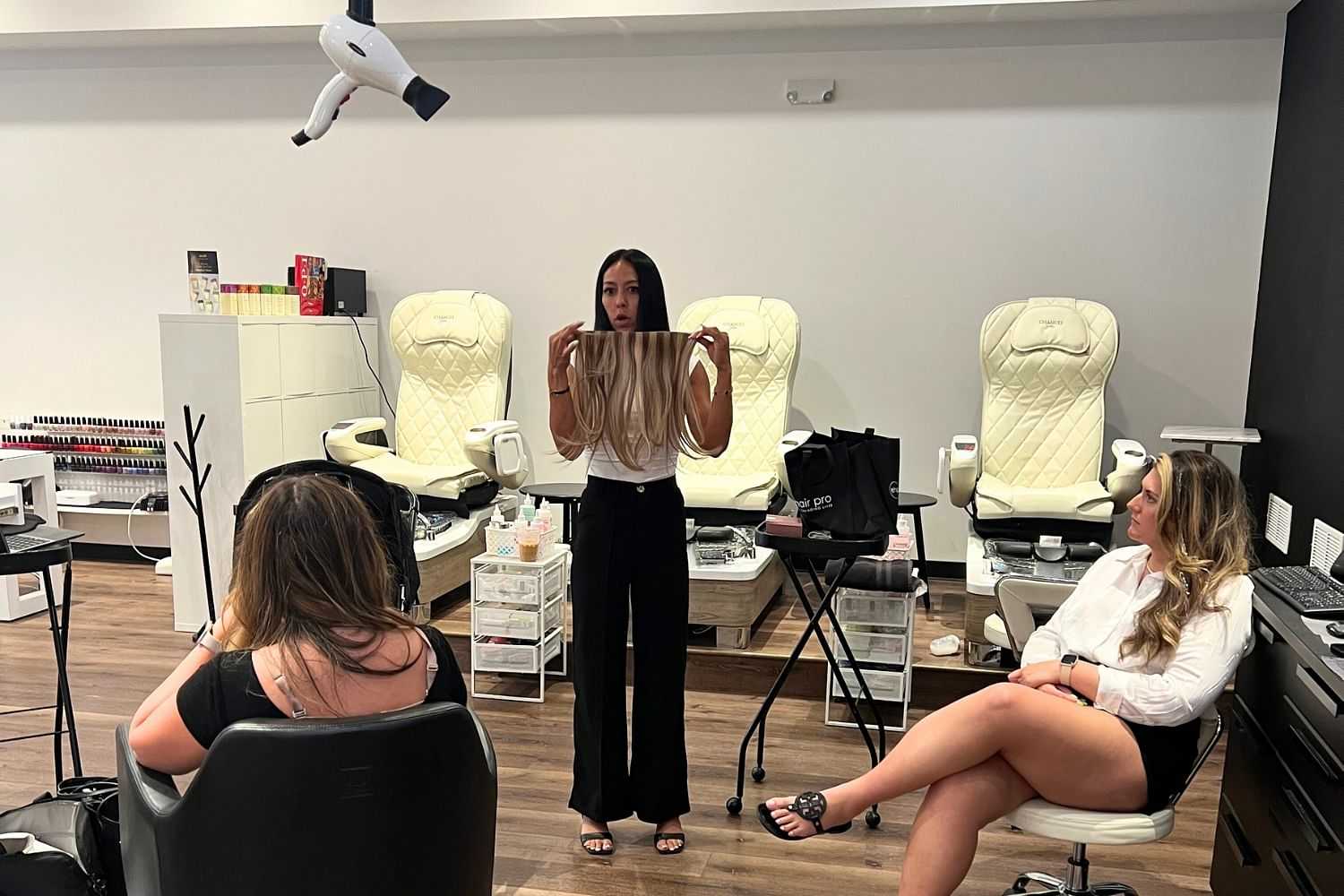 Hairstylist demonstrating hair extensions to clients in a modern salon setting.